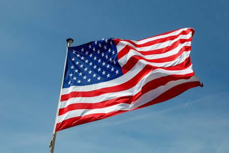 View of the national flag of the United States of America flying on a flagpole against a sunny sky.の写真素材