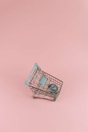 Planet earth glued to duct tape, placed in a blue shopping chart on a light pink background. Contemporary minimal environment and anti consumerism photo.の写真素材