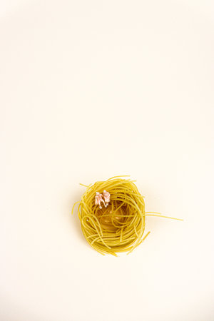Yellow Pasta for soup in shape of circle with two miniature persons seating on it, on a beige background. Contemporary minimal food photo of agriculture producers or cooks.の写真素材