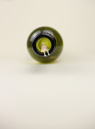 Miniature man seating in the dark green wine bottle, on a beige background.の写真素材