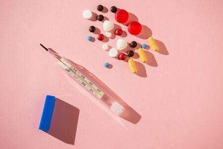 Medical thermometer and colorful pills on pink backgroundの写真素材