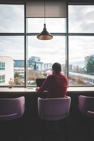 Freelancer man with red shirt with glasses working on laptop in coffee shop by the window, remote workの写真素材