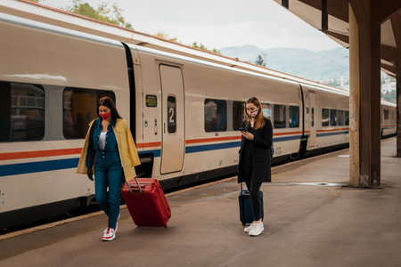 Woman friends waiting a train, with face mask and bagsの写真素材