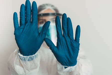 Healthcare worker with shield and mask showing stop gestureの写真素材
