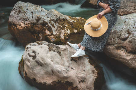 woman with hat sitting on the rocks on the river stream in the forestの写真素材
