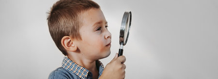 Little boy looking through a magnifying glass on a gray background.の写真素材
