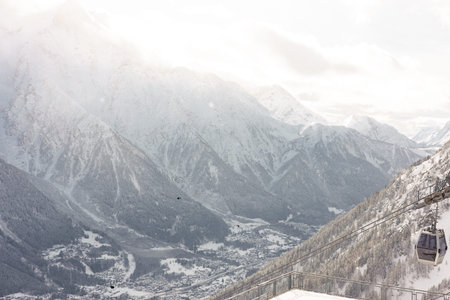 Snowy mountain landscape with cable car and village in winter, cold weather, scenic alpine scenery, cable transport, tranquil atmosphereの写真素材