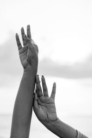 Black and white image of two hands reaching upwards, symbolizing hope, unity, and empowerment against a cloudy sky backgroundの写真素材