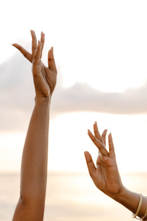 Elegant hands reaching towards the sky during sunset, capturing freedom, grace, and serenity at the beachの写真素材