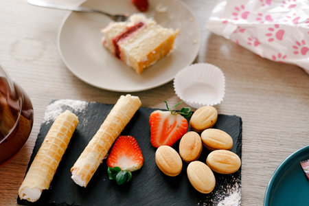 Delicious assorted cookies and fresh strawberries on a slate serving board with cake in the backgroundの写真素材