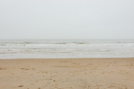 Calm, misty beach scene with sandy shore, gentle waves, overcast sky, soothing mood, minimalistic coastal landscapeの写真素材