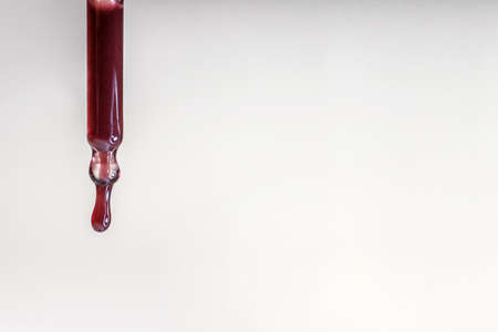 A drop of red serum drops from the pipetteの写真素材