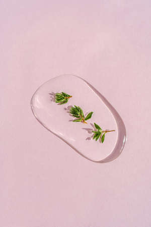 A drop of cosmetic gel with thyme on a pink background.
