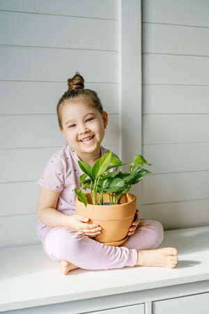 The girl is sitting on the dresser with a flower pot.の写真素材