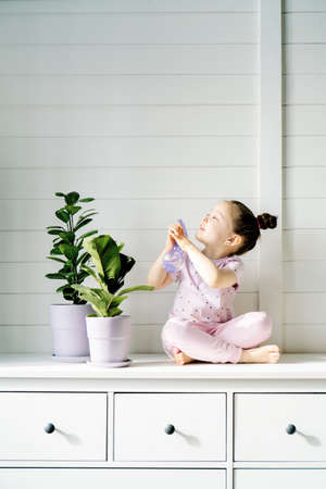 The girl is sitting on the dresser next to two flower pots.の写真素材