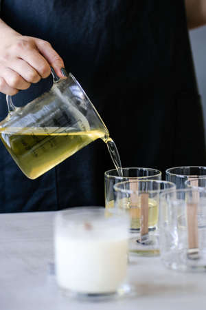 The girl pours wax into glass glasses with wicks.の写真素材