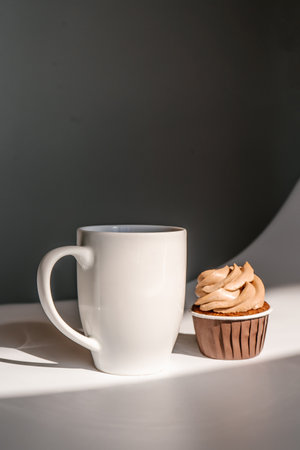 A cupcake or muffin stands next to a cup of coffee.の写真素材