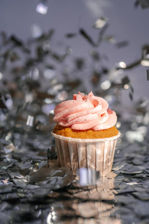 A cupcake with a pink cap stands among the flying silver confetti.の写真素材