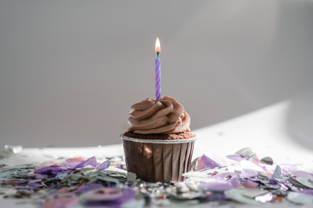 A cupcake with a candle stands on a white background with a shadow.の写真素材