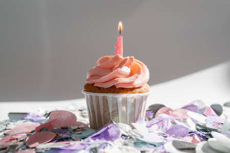 A cupcake with a candle stands on a white background with a shadow.の写真素材