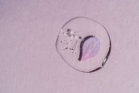 A drop of transparent cosmetic gel with flowers on a purple background.