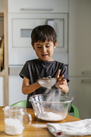 The child cooks in the kitchen. Sifts the flour.の写真素材