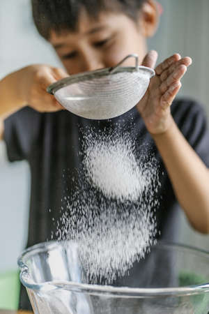 The child cooks in the kitchen. Sifts the flour.の写真素材