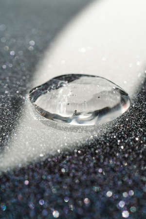 A drop of cosmetic gel on a black shining background.