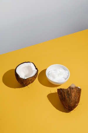 Two halves of coconut and coconut oil in a bowl.の写真素材