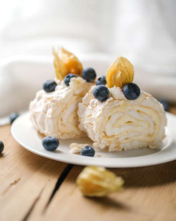 Two pieces of meringue roll with berries on a white plate on a wooden table.