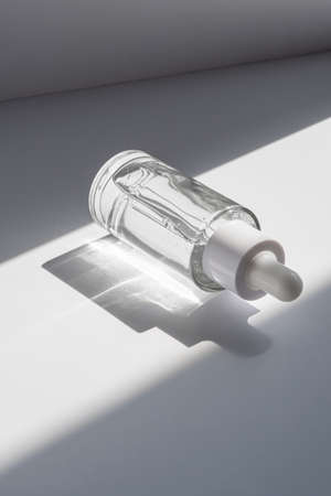A white transparent bottle with serum in the rays of the sun.