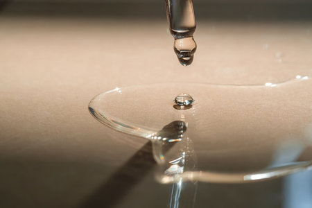 A Dripping Pipette of cosmetic gel on a beige background.