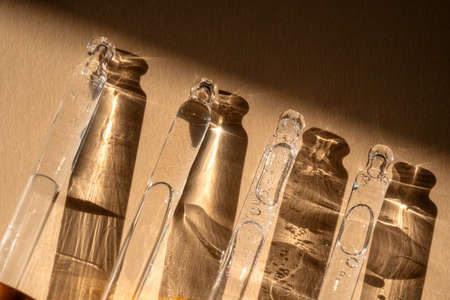 Four pipettes of cosmetic gel on a beige background.