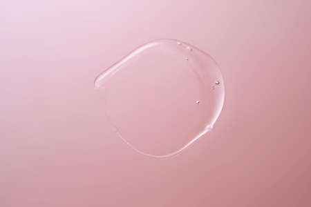 Drop of cosmetic transparent gel on a pink background. The texture of the serum, heir gel or...