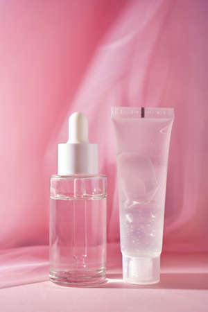 A transparent bottle of cosmetic gel and a bottle of serum on a pink background.