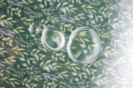 Three drops of cosmetic transparent gel on a green background. The texture of the serum.の写真素材
