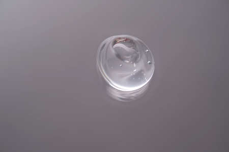 Drop of cosmetic transparent gel on a grey background. The texture of the serum, heir gel or hyaluronic booster.の写真素材