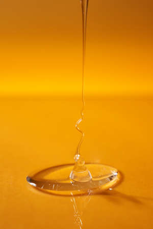 A drop of body gel or shampoo pouring from above on a yellow saturated background.