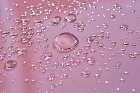 A large drop and splashes of micellar water on a pink background.の写真素材