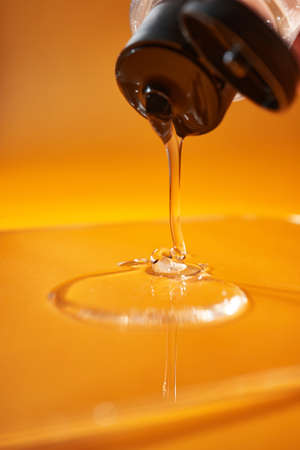 A drop of body gel or shampoo pouring from above on a yellow saturated background.