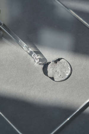 Pipette with spilled cosmetic oil or serum on a gray background.