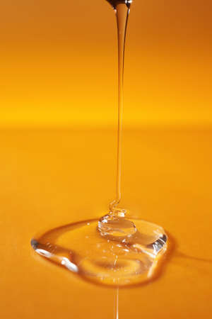 A drop of body gel or shampoo pouring from above on a yellow saturated background.の写真素材