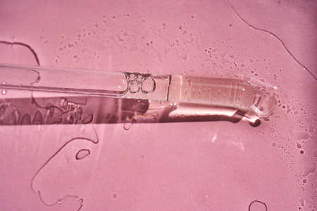 Dropper with serum or cosmetic oil on a pink background.