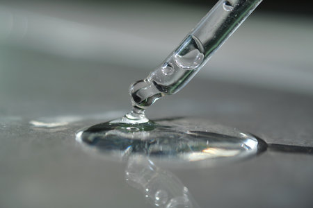Pipette with spilled cosmetic oil or serum on a gray background.
