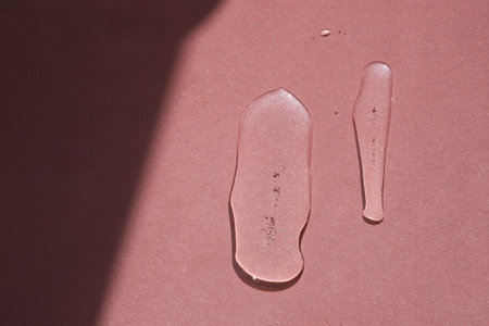 Two elongated drops of cosmetics or perfume of a plant on a pink background.の写真素材