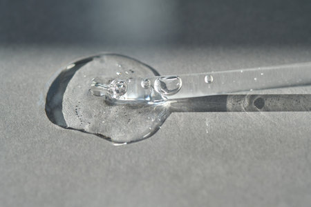 Pipette with spilled cosmetic oil or serum on a gray background.