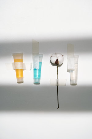 Cosmetics of different colors and a sprig of cotton on a white background with tape.の写真素材