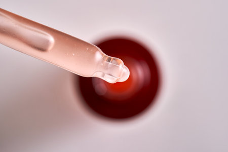 Pipette with pink cosmetic product on the background of a burgundy bottle.