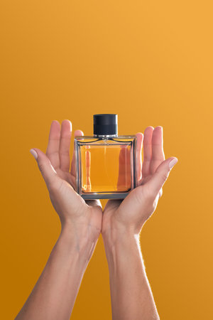 Perfume bottle in hands on an orange background.の写真素材