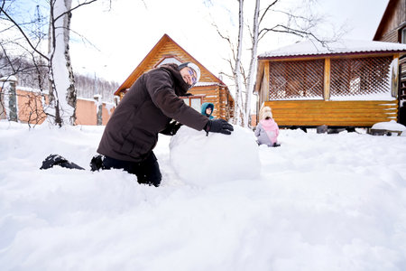 A family builds a snowman out of white snow in the yard in winter.の写真素材